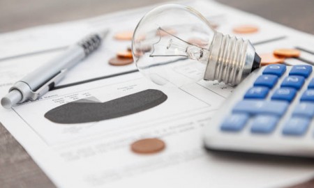 A light bulb, a pen, a calculator and some copper euro cent coins lie on top of an electricity bill.